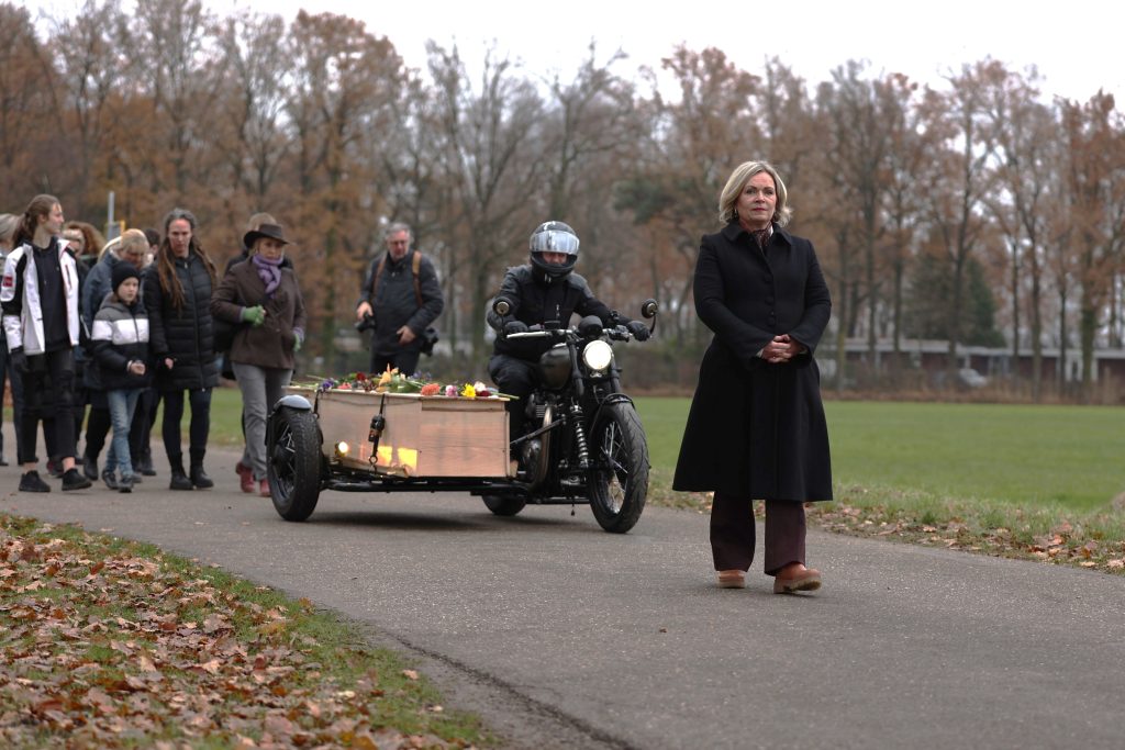 Leny_5 Laatste groet van twee mensen bij de kist voor het sluiten omringd door gekleurde bloemen bij het raam