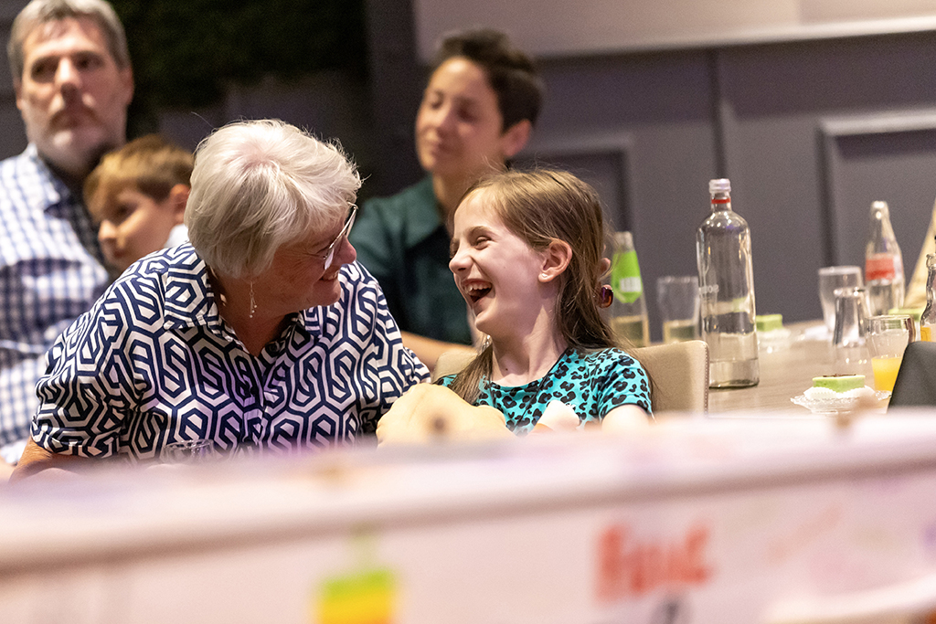 GonnieBax5 Familie kijkt met lach naar foto buiten beeld in een uitvaart ceremonie, voorop een baar met wade.