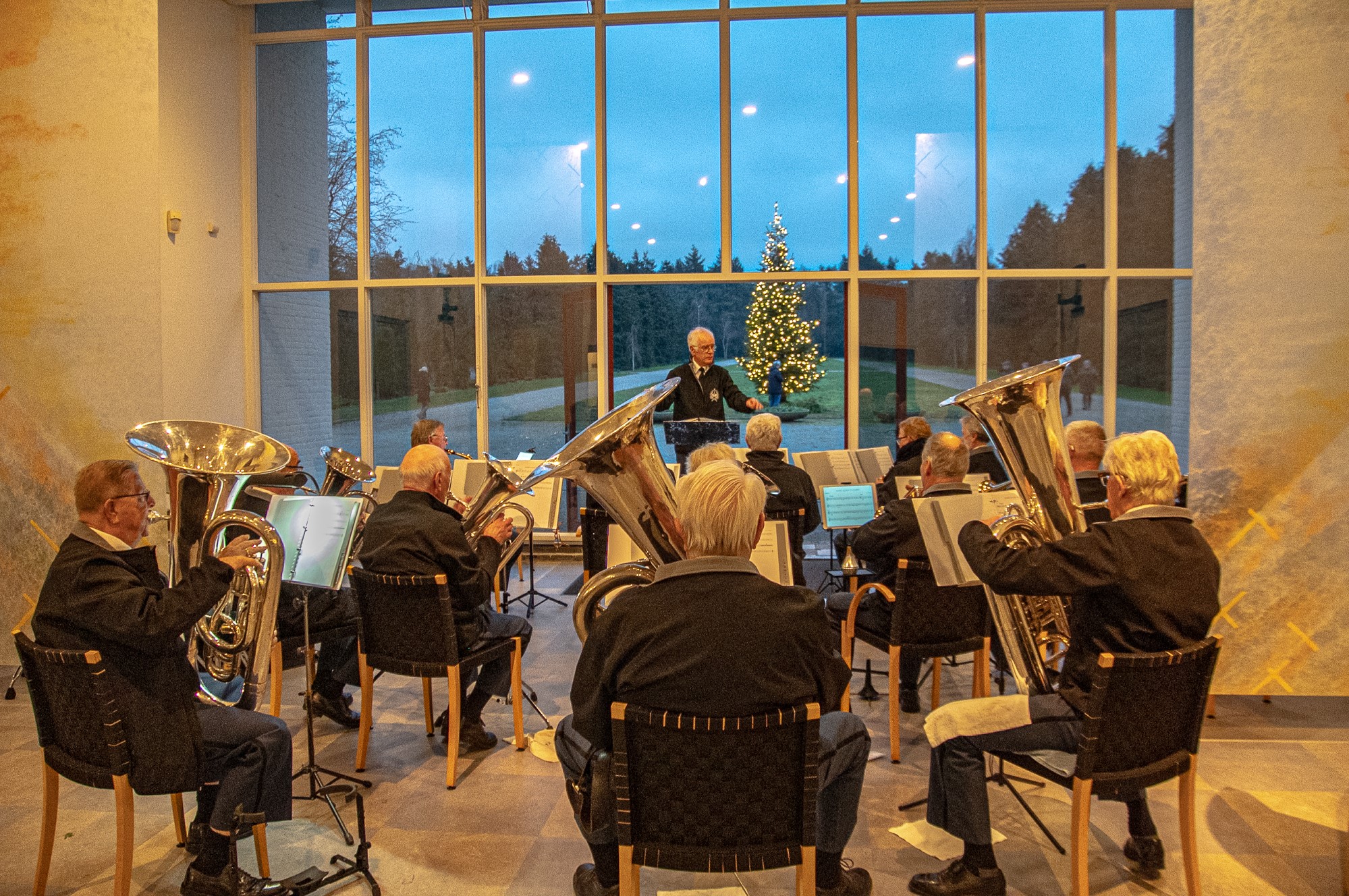 Muziekorkest met blazers voor het raam met een kerstboom op de achtergrond buiten